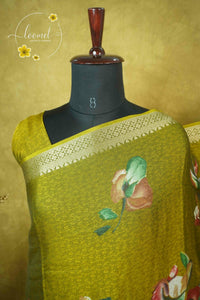 ARN21002 Mustard-green saree features artistic hand-painted floral patterns, a gold zari border, and an intricate traditional elephant-motif pallu.
