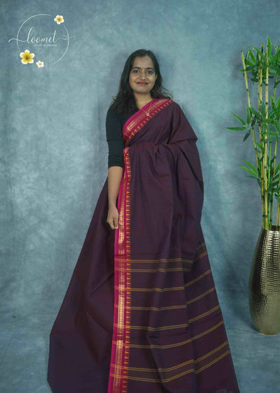 NLS1113 Deep plum saree features a solid body with a vibrant pink border, decorated with colourful temple patterns and golden Zari.
