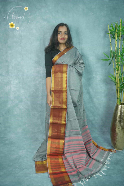 NLS1117 Light grey saree features a solid body and a wide golden zari border with intricate checked and temple patterns.